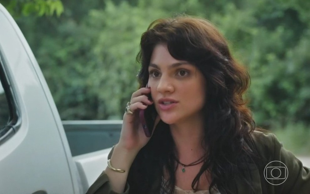 A atriz Debora Ozório segura celular e fala em cena da novela Terra e Paixão como a personagem Petra