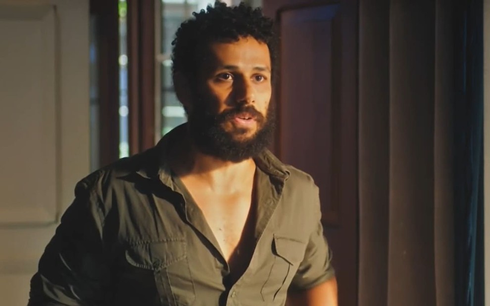 Amaury Lorenzo caracterizado como Ramiro; ele usa uma camisa verde semiaberta e parece tenso em cena de Terra e Paixão