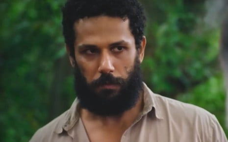 Amaury Lorenzo caracterizado como Ramiro; ele usa uma camisa bege e parece tenso e confuso em cena de Terra e Paixão