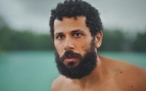Amaury Lorenzo caracterizado com Ramiro; ele está com os olhos arregalados e a boca aberta enquanto toma banho de rio em cena de Terra e Paixão