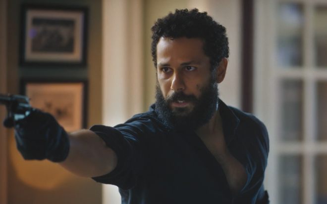 O ator Amaury Lorenzo segura arma e aponta para alguém em cena da novela Terra e Paixão