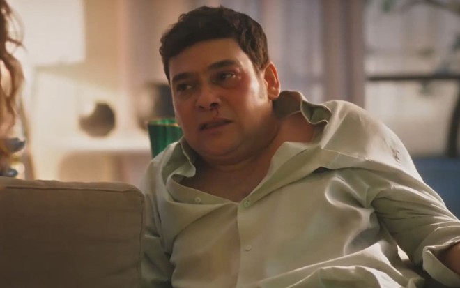 Claudio Gabriel caracterizado como Tadeu; ele usa uma camisa social branca e tem o rosto ferido em cena de Terra e Paixão