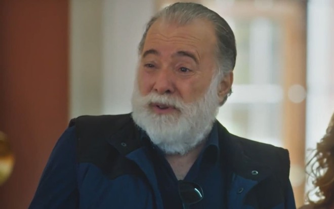 Tony Ramos caracterizado como Antônio; ele usa um casaco preto e exprime deboche em cena de Terra e Paixão