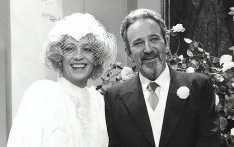 Vestido de noiva, Ney Latorraca sorri ao lado de Carlos Kroeber, que usa terno e gravata