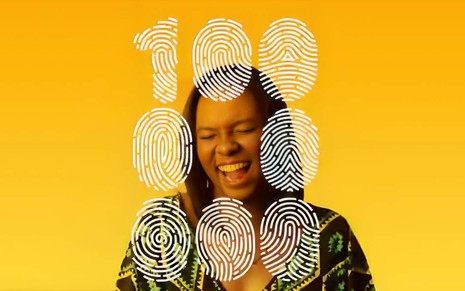 Imagem de vídeo da campanha 100 Milhões de Uns, lançada pela Globo em 2017: uma jovem negra sorri sob a impressão do número 100.000