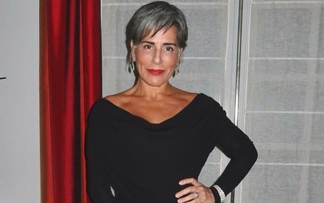 Gloria Pires usa um vestido preto de mangas longas, cabelos curtos e grisalhos e um batom vermelho