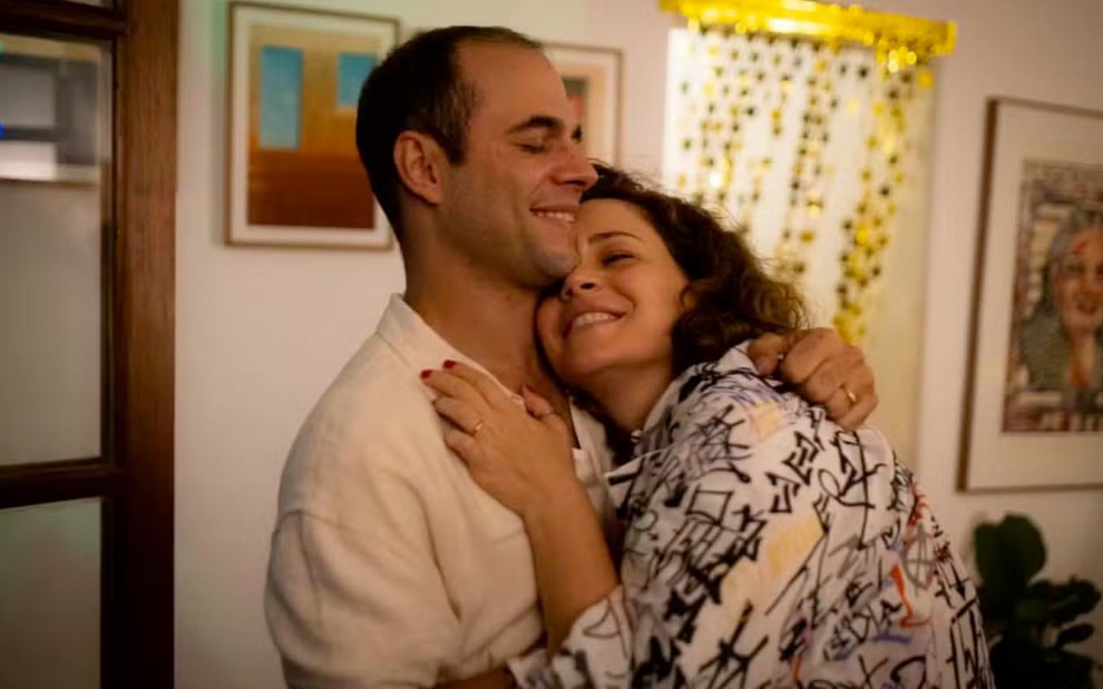 Guilherme Burgos abraça Leandra Leal dentro de um apartamento à meia luz