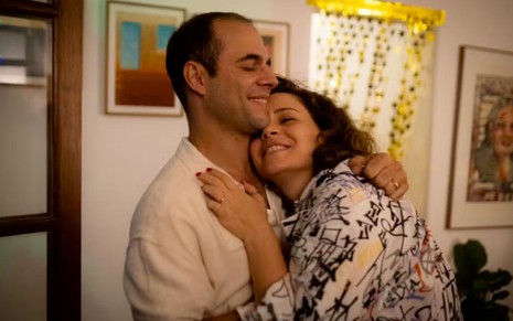 Guilherme Burgos abraça Leandra Leal dentro de um apartamento à meia luz