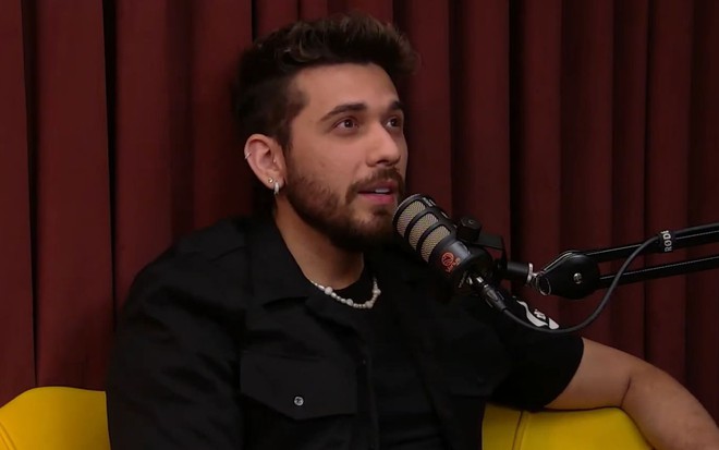 O cantor Gustavo Mioto em frente a um microfone durante um podcast