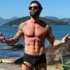 Gusttavo Lima está sem camisa, de braços abertos e usa óculos de sol; ao fundo é possível ver o mar e uma ilha