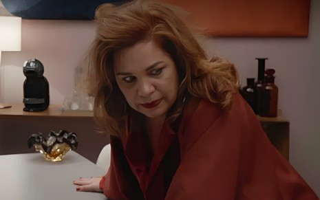 A atriz Isabel Teixeira com expressão perturbada, debruçada sobre mesa, em cena de Elas por Elas
