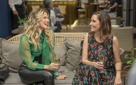 Em cena de Bom Sucesso, Ingrid Guimarães está ao lado de Claudia Souto em um sofá; ambas têm uma taça de bebida nas mãos