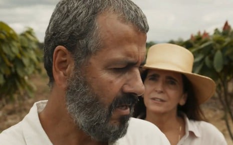 Em cena de Renascer, Marcos Palmeira está conversando com Malu Mader, que está atrás dele usando chapéu