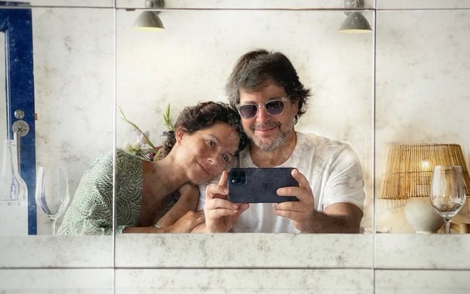 Cecília Malan apoia cabeça no ombro de Murilo Benício, que tira selfie dos dois em espelho sujo