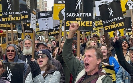 Atores gritam em protesto e erguem os braços; alguns têm placas de apoio ao SAG-AFTRA, sindicato dos artistas