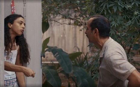 Em cena de Renascer, Alice Carvalho está no batente da porta, conversando com Irandhir Santos, que está do lado de fora