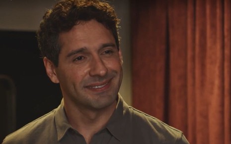 Em cena de Família É Tudo, João Baldasserini está sorrindo, olhando para alguém