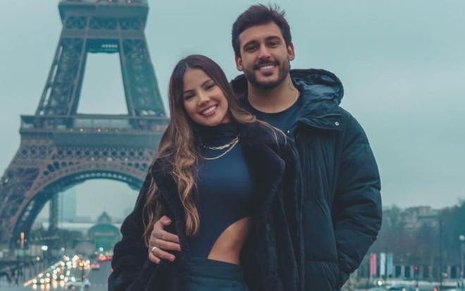 Luana Andrade e João Hadad estão abraçados, com a Torre Eiffel ao fundo