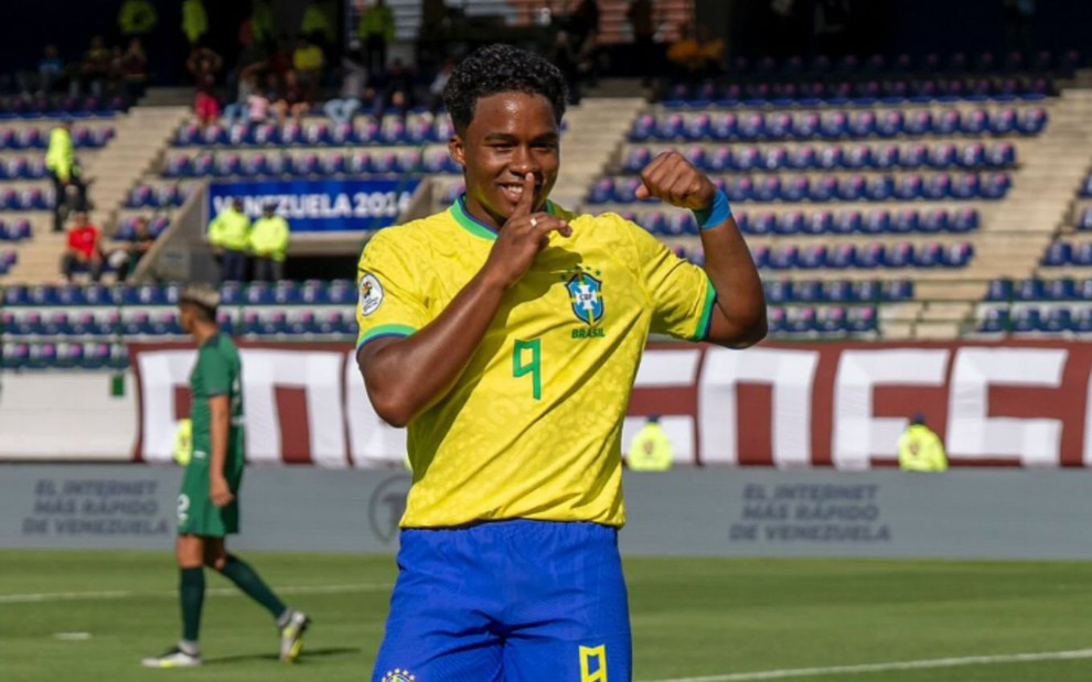 Imagem colorida mostra o jogador Endrick vestido com o uniforme da seleção brasileira e segurando uma bola na mão