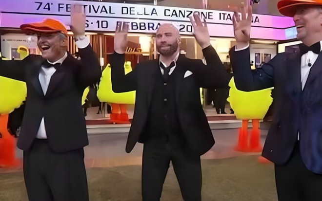John Travolta de terno e gravata fazendo a dança do passarinho durante transmissão de festival de música na Itália