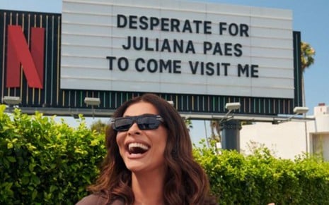 Juliana Paes em frente a um outdoor em que se lê: desperate for Juliana Paes to come visit me