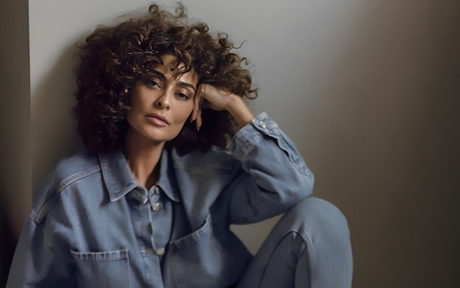Juliana Paes posa para foto sentada no chão; ela tem os cabelos bem enrolados e apoia a cabeça na mão