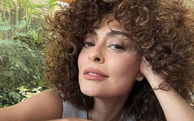 Juliana Paes posa para a foto com a cabeça apoiada na mão esquerda; ela está com o cabelo cacheado