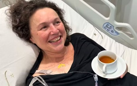 Kelzy Ecard deitada em um leito hospitalar com uma xícara de chá
