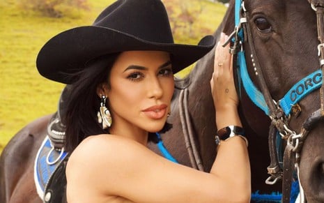 Foto de Larissa Tomásia; ela usa chapéu de fazendeiro e está ao lado de cavalo