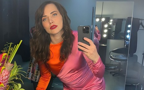 Com um vestido rosa e laranja, Letícia Colin faz uma foto com o próprio celular em um espelho