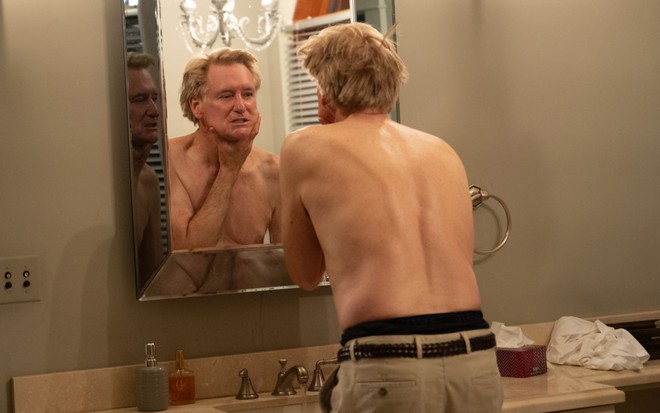 Sem camisa, Bill Pullman se olha no espelho enquanto faz careta em cena do filme Assassinatos na Família Murdaugh