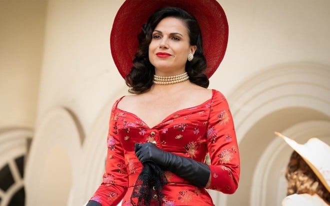 Lana Parrilla tem um sorriso malicioso em cena de Why Women Kill; ela usa um vestido decotado vermelho