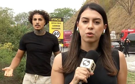 MC Livinho está com expressão confusa; na frente a repórter Isabela Campos segura microfone da Globo