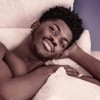 Sem camisa, Lil Nas X está deitado em uma cama e tem expressão doce