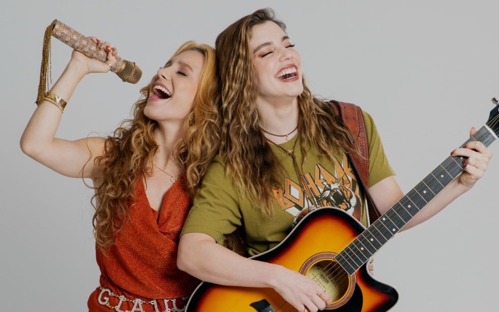 Gláucia (Lorena Comparato) canta em microfone, e Raíssa (Alice Wegmann) segura um violão em foto de Rensga Hits!