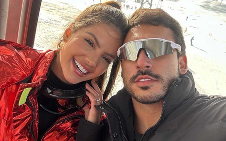 Luana Andrade e João Haddad lado a lado, em foto durante viagem a lugar com neve, ela sorrindo e ele sério, de óculos de sol