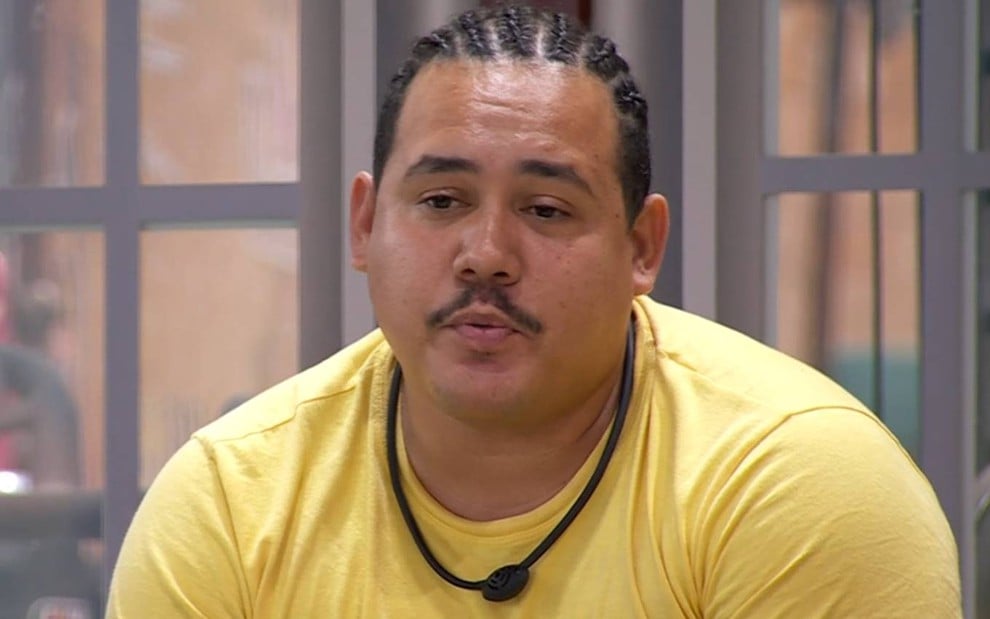 Foto de Lucas Henrique no BBB 24; ele veste camiseta amarela e usa microfone no pescoço