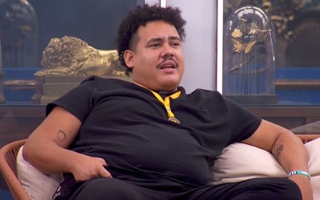 Lucas Henrique Ferreira usa uma camiseta preta e está sentado na varanda do BBB 24