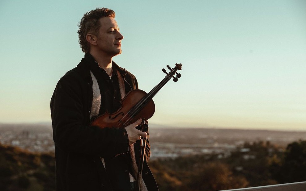 Lucas Lima segura violino e tem expressão séria em foto contemplativa de montanhas