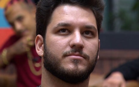 Um homem branco, de cabelo preto e barba preta, com uma expressão triste