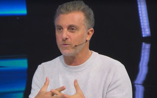 Luciano Huck no palco do Domingão com Huck usando uma blusa branca