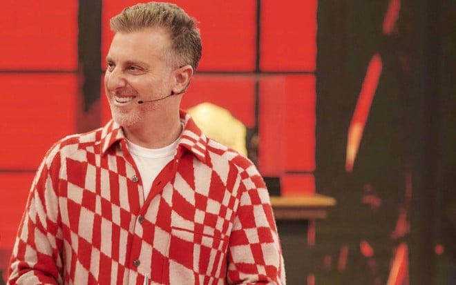 De camisa branca e vermelha, Luciano Huck está no palco do Domingão com Huck