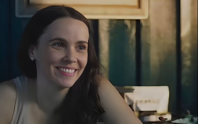 Em cena de Terra e Paixão, Débora Falabella está sorrindo, faland com alguém