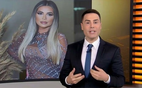 Luiz Bacci está vestido com um terno no Cidade Alerta, na Record, com a foto de Deolane Bezerra em um telão ao fundo