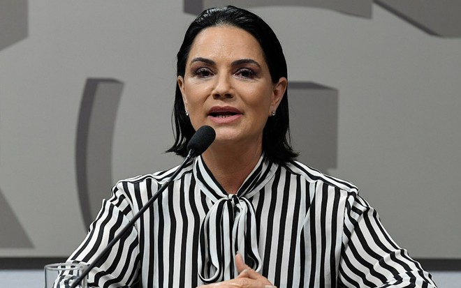Luiza Brunet está sentada numa bancada e discursa, com um microfone próximo à boca
