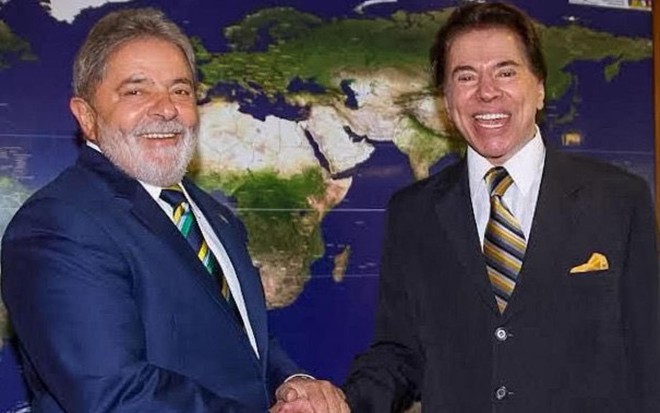 Luiz Inácio Lula da Silva e Silvio Santos de mãos dadas, sorrindo para câmera