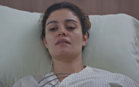 Sophie Charlotte com expressão séria e deitada em cama de hospital em cena como Maíra na novela Todas as Flores