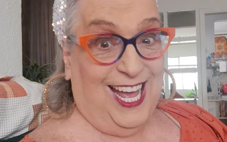Mamma Bruschetta usa uma camiseta laranja e um óculos com aro da mesma cor; ela sorri para a câmera