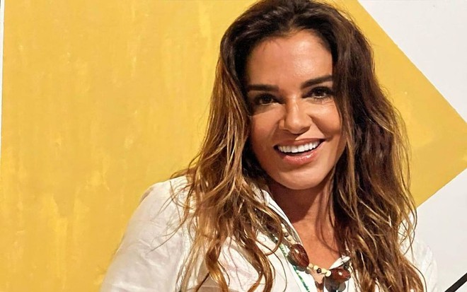 A atriz Mara Carvalho posa para foto sorrindo, com camisa branca, deixando barriga aparecer