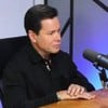 Foto de Marcão do Povo durante entrevista; ele veste camiseta preta e está próximo a um microfone